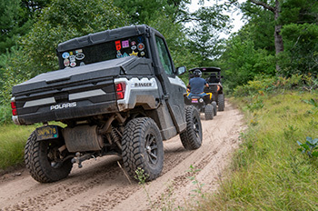 Three ORVs riding on natural surface trail through woods