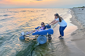 Julie Wernette accompanies Jamie Spore, seated in a floating accessible beach chair, along the Lake Michigan shoreline at Ludington State Park