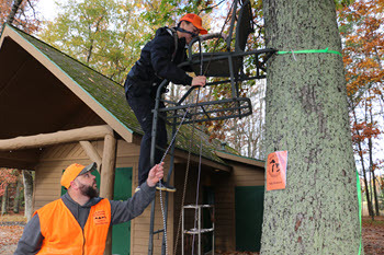 An adult helps a youth hunter into a tree stand.