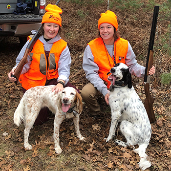 Two hunters clad in blaze orange pose with their hunting dogs