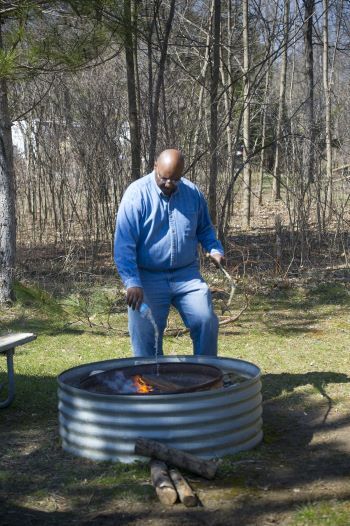 A man uses water and a stick to drench and stir a campfire to make sure it is out. 