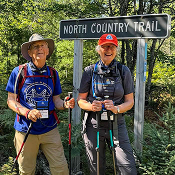 A couple posing for a photo along the trail. A North Country Trail sign is behind them.