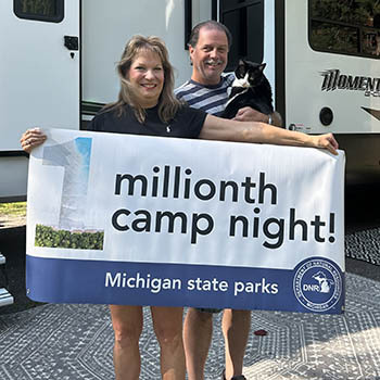 a couple holding a cat and 1 millionth camp night banner