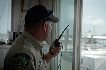 a harbormaster with radio looking out window into harbor