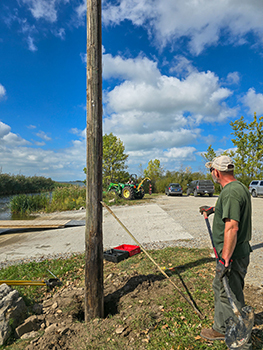 A worker is shown on the project to install a light at the boating access site.