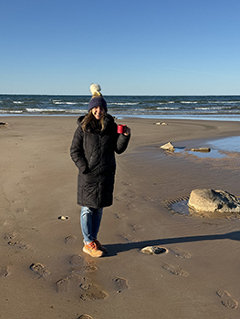 person walking on beach with coffee in cold weather