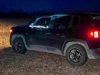 The barrel of a gun is shown sticking out of a truck window after dark.