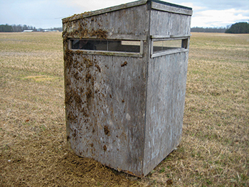 A deer blind fouled with manure is shown standing in an open field.