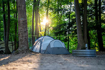 a tent and firepit with sun peeking through trees