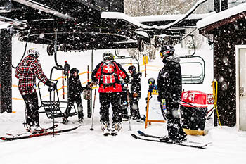 Snow falling around people getting on ski lift