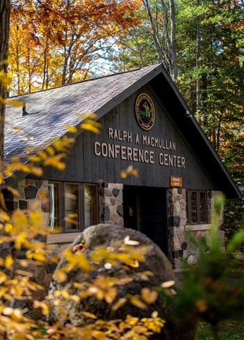 the brown and stonework visitors building of the Ralph A. MacMullan Conference Center, framed by gold and orange autumn leaves