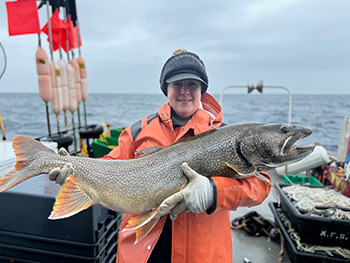 A DNR research technician with a large lake trout caught during survey at Isle Royale, June 2024.