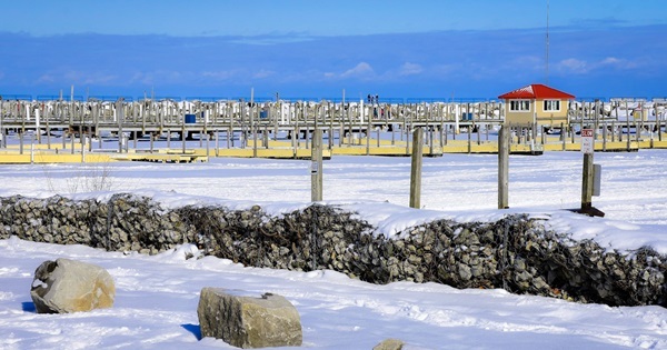 People on the pier at Lexington State Harbor, with the snow-covered breakwall in the foreground and bright blue winter sky behind