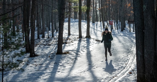 a lone runner in black leggings, jacket on the snowy, foggy VASA Pathway, as sunlight streams through the trees in background