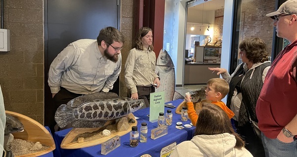 a man and woman in U.S. Fish and Wildlife Service attire show bighead carp models and anatomy to kids at an invasive species expo