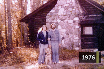 old photo of couple standing in front of rustic cabin, dated 1976