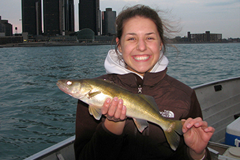 angler holds walleye with Detroit River and skyline in background