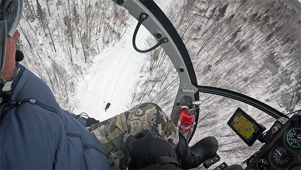 A view from a helicopter shows moose operations taking place below on the snow-covered landscape.