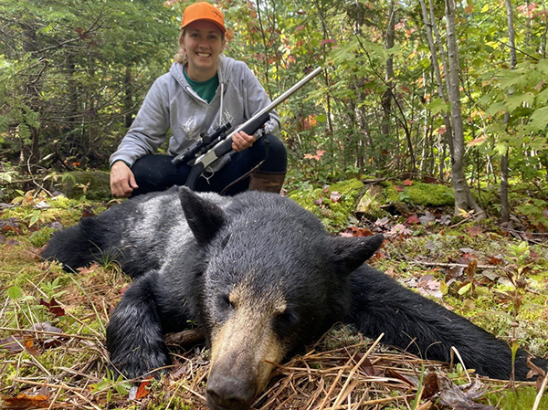 Sara Brown poses for a picture in the woods with the black bear she harvested.