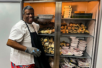 A Hunters Feeding Michigan volunteer stands in front of an open refrigerator door, smiling.