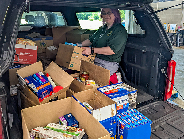 The author is shown sitting in the back of a vehicle with food donation items.