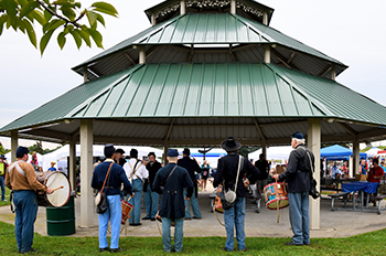 A group of people around a pavilion, some in historic costumes.