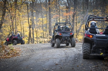off-road vehicles ride single-file down a state forest road amid autumn-hued trees near Marquette, Michigan
