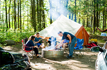 a family sitting around campfire with tent in background