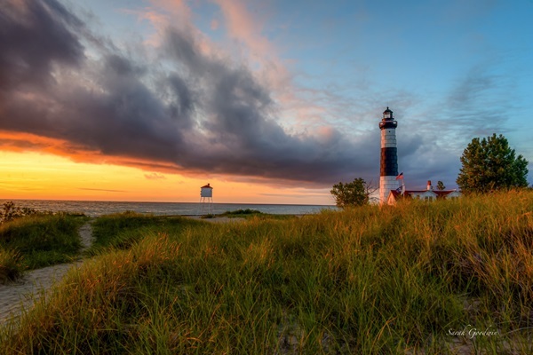 black and white Big Sable Point Lighthouse perched on a grassy rise overlooking Lake Michigan, with gray clouds giving way to orange light