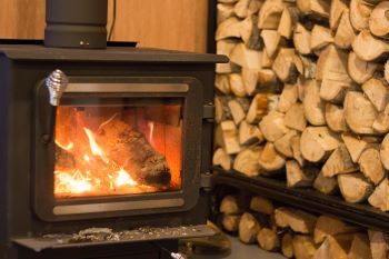 A merrily blazing traditional black wood stove sits next to a stack of neatly split and well-dried firewood. 