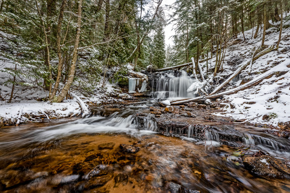 Wagner waterfalls shows a gently cascading waterfall with light snow on forested land around it.