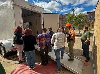 Participants in the deer processing event crowd around the back of a freezer truck to learn about processing.