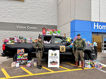two conservation officers in front of patrol truck full of toys