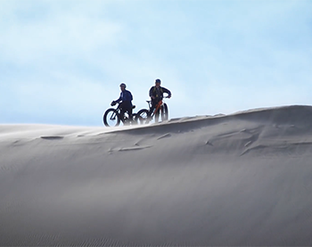 two fat-tire bikers posed on top of a snow dune
