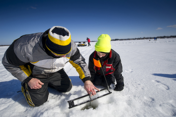 adult teaching child about ice fishing on frozen lake