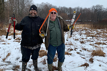two volunteers in winter holding tools for invasive species removal