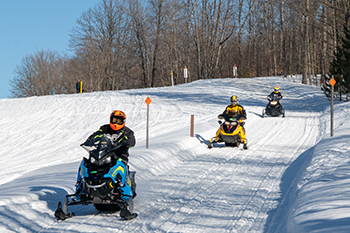 three snowmobile riders on trail