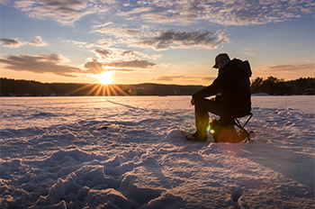 an angler sittingo on a bucket ice fishing