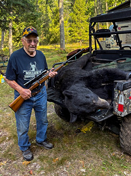 Milton Miller stands with his gun, and his harvested bear is shown in the back of Miller's all-terrain vehicle.