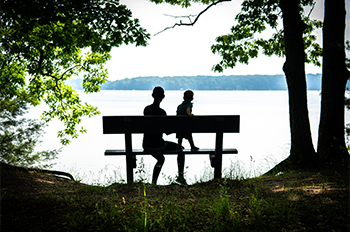 silhouettes of mother and child on bench overlooking lake
