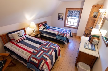 Colorful quilts and nautical pillows on beds, knotty pine floors, a dresser in a bedroom of Tawas Point Lighthouse keeper's quarters