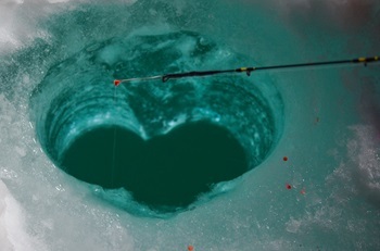 a thin, black fishing rod perched over a heart-shaped fishing hole cut into several-inches-thick, blue-white ice