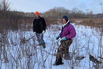 Man and woman dressed in winter hats, coats and pants, holding pruning shears, volunteering to clean up state park natural areas