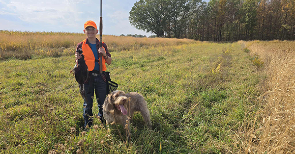 young hunter in field holding harvested pheasant
