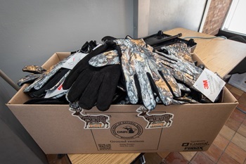 a cardboard box overflows with dozens of pairs of black, tan and camouflage-patterned deer-skin gloves