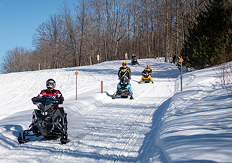 four spaced-apart snowmobiles riding on trail
