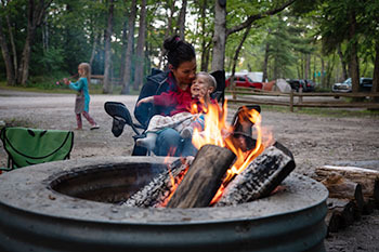 a mother and child sitting at the campfire in a campground