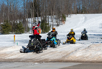 group of snowmobilers get ready to cross a road