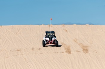 an off-road vehicle with an orange flag comes over a sand dune at Silver Lake State Park on a sunny day