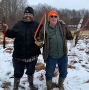 Two smiling volunteers holding hand tools in the winter time
